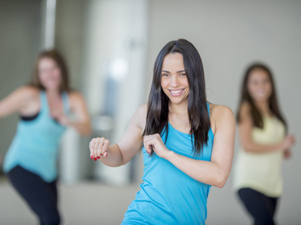 一群多民族的年轻女性正在健身房一起上舞蹈健身课。他们随着音乐起舞，看着镜头微笑。
