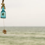 一个空的，水蓝色的瓶子挂着一个贝壳作为夏天的风铃装饰和风铃-拍摄在一个下午，以海岸为背景。