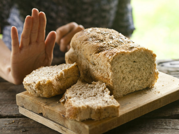 一个拒绝面包和无麸质概念的女人。一条全麦面包放在一张质朴的木桌上，一个女人用手势拒绝它。