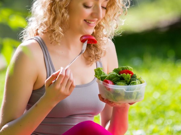 年轻苗条的女人拿着一碗新鲜的沙拉后，在公园户外锻炼。吃着新鲜的空气，坐在草地上，享受清晨。健康的生活方式。