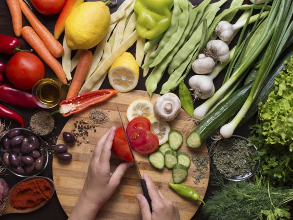 用手在砧板上切生蔬菜，周围是蔬菜和香料