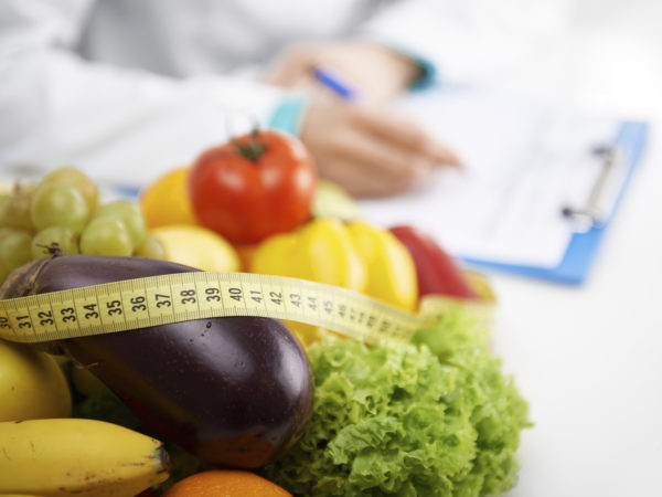 健康营养的概念。特写新鲜蔬菜和水果与测量卷尺躺在医生的桌子上。