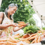 一位50多岁的老妇人在当地农贸市场购买新鲜的有机蔬菜。她微笑着选择胡萝卜。具有复制空间的水平图像。