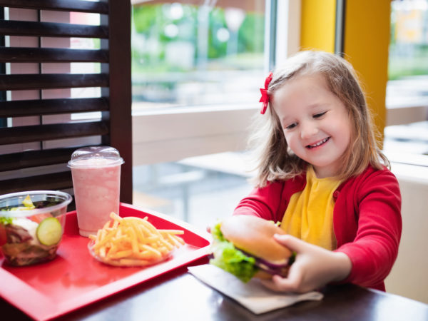 小女孩在快餐店吃汉堡包和炸薯条。孩子午餐吃三明治和薯片。孩子们吃不健康的油腻食品。儿童烧烤快餐三明治。