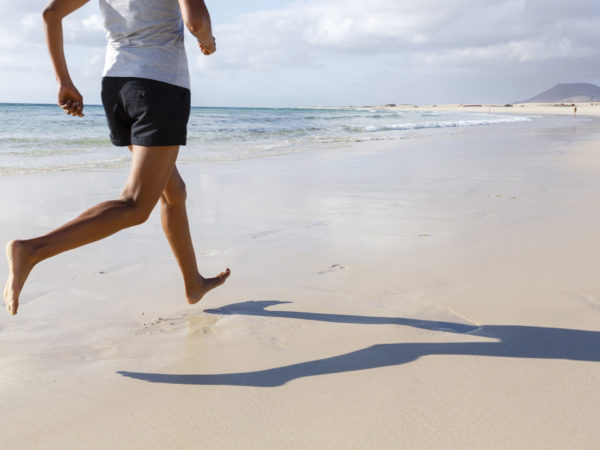 适合的亚洲跑步者在沙滩上赤脚慢跑
