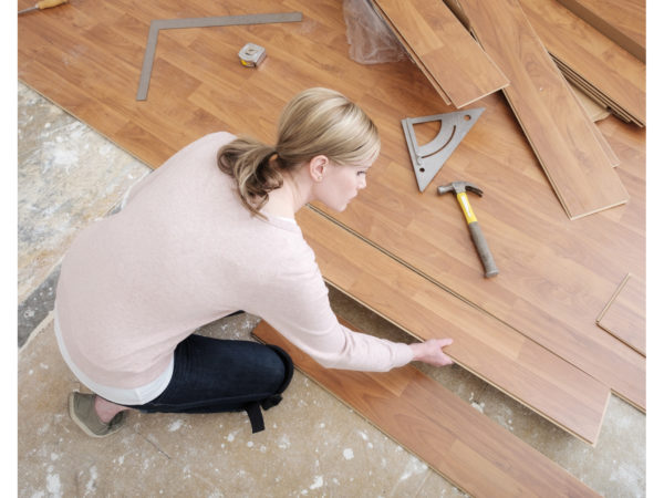 一名妇女正在自己的家里做一个安装强化木地板的diy项目。从上面看，她正在放木板。