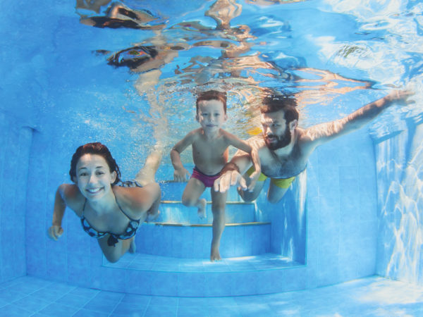 幸福的家庭——爸爸妈妈带着小男孩在蓝色的水池里游泳和潜水，玩得很开心。健康的生活方式，积极的父母，和人们在暑假与孩子水上运动活动