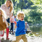 在一个美好的夏日，一家人坐在湖边。孩子们跑在前面，父母在一旁看着。