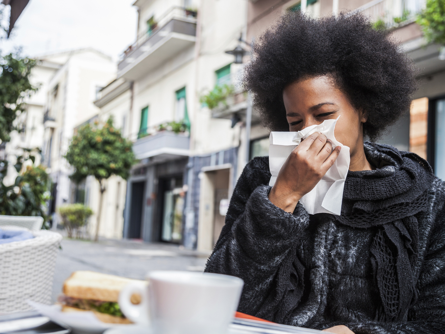 一名妇女在咖啡馆休息时用手帕打喷嚏，因为流感