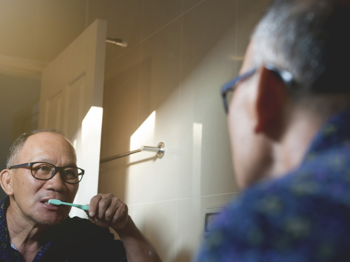 亚洲老人正在浴室里刷牙和照镜子。