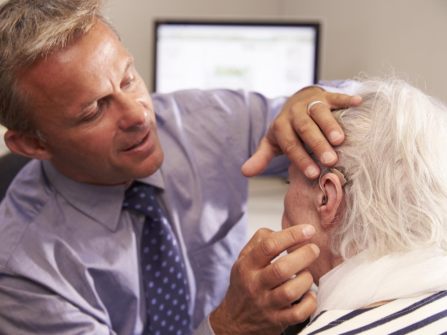 医生为老年女性患者配戴助听器