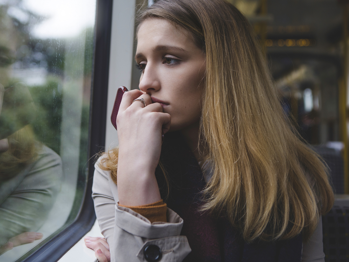 年轻女子坐在火车上，看着窗外，看起来很沮丧。她把手机举到嘴边。