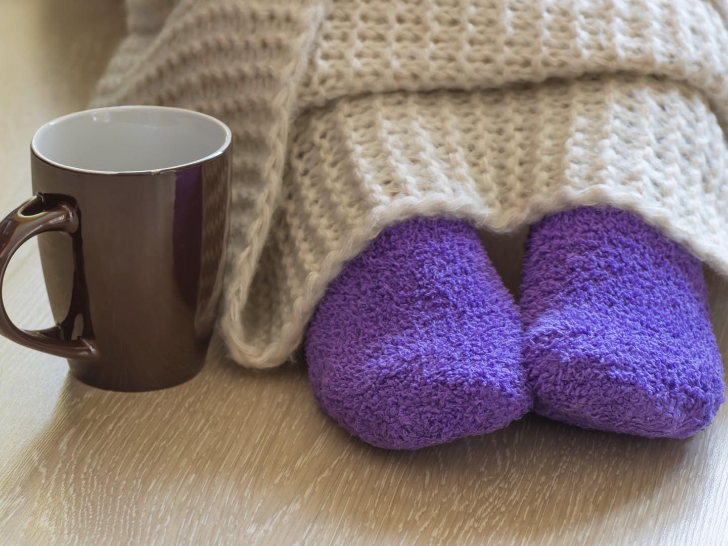 冷的概念与茶杯附近的腿，覆盖着蓬松温暖的毯子和穿着蓬松温暖的紫色袜子