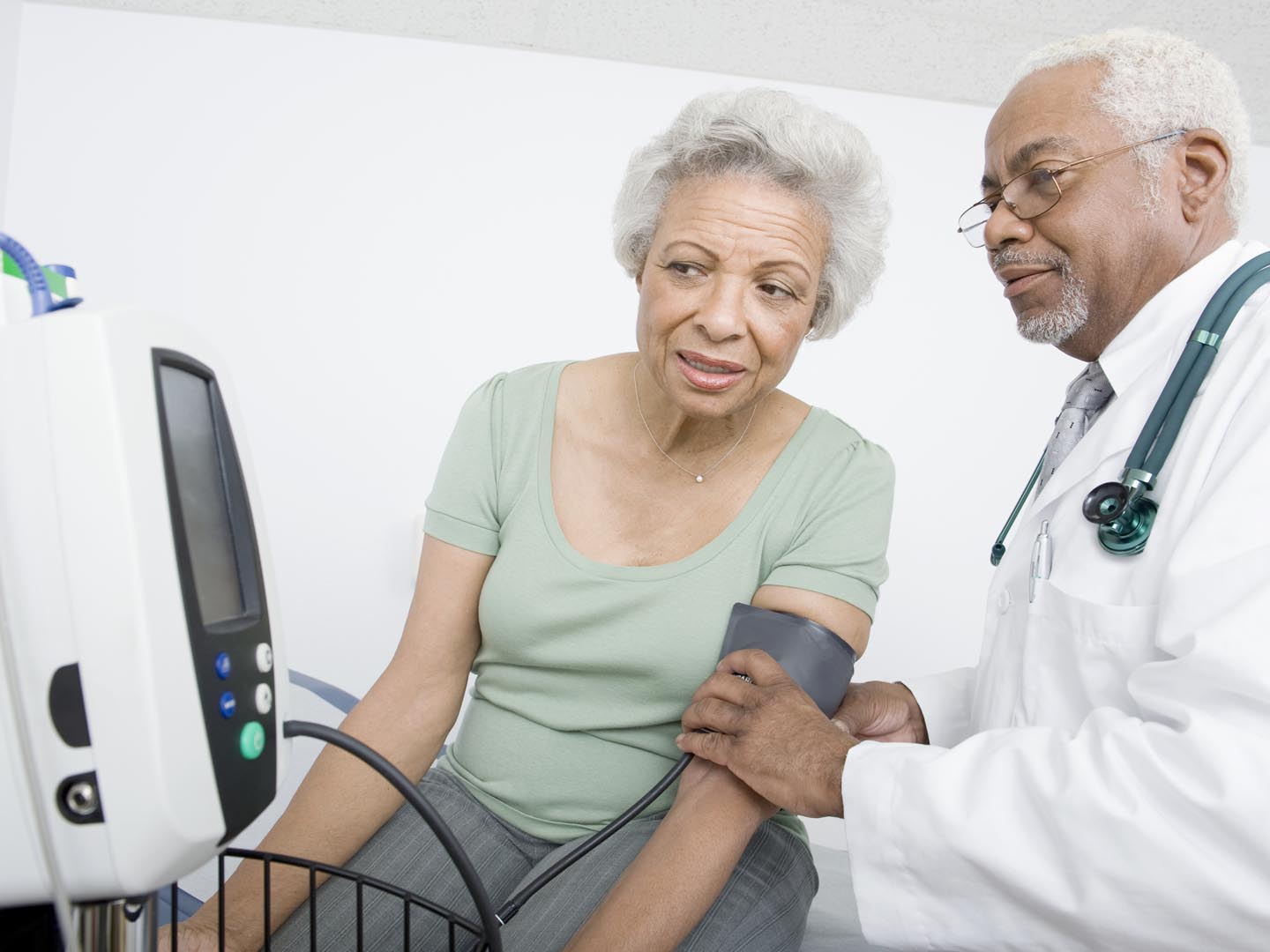 男医生在诊所边看仪器边给病人量血压