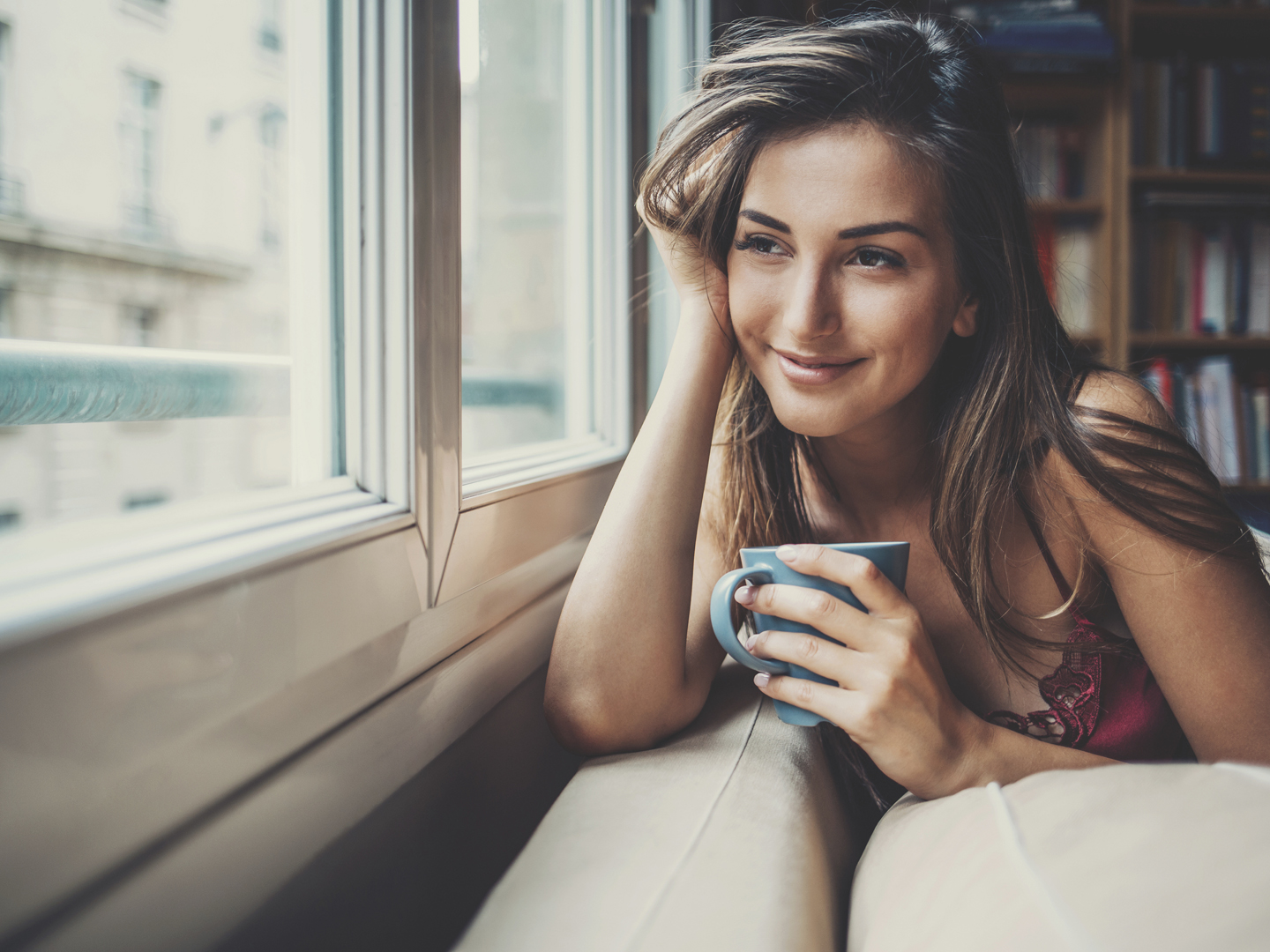 美丽的年轻女子拿着一杯咖啡，透过房子的窗户往外看。拍摄于2016年巴黎Istockalypse活动期间。