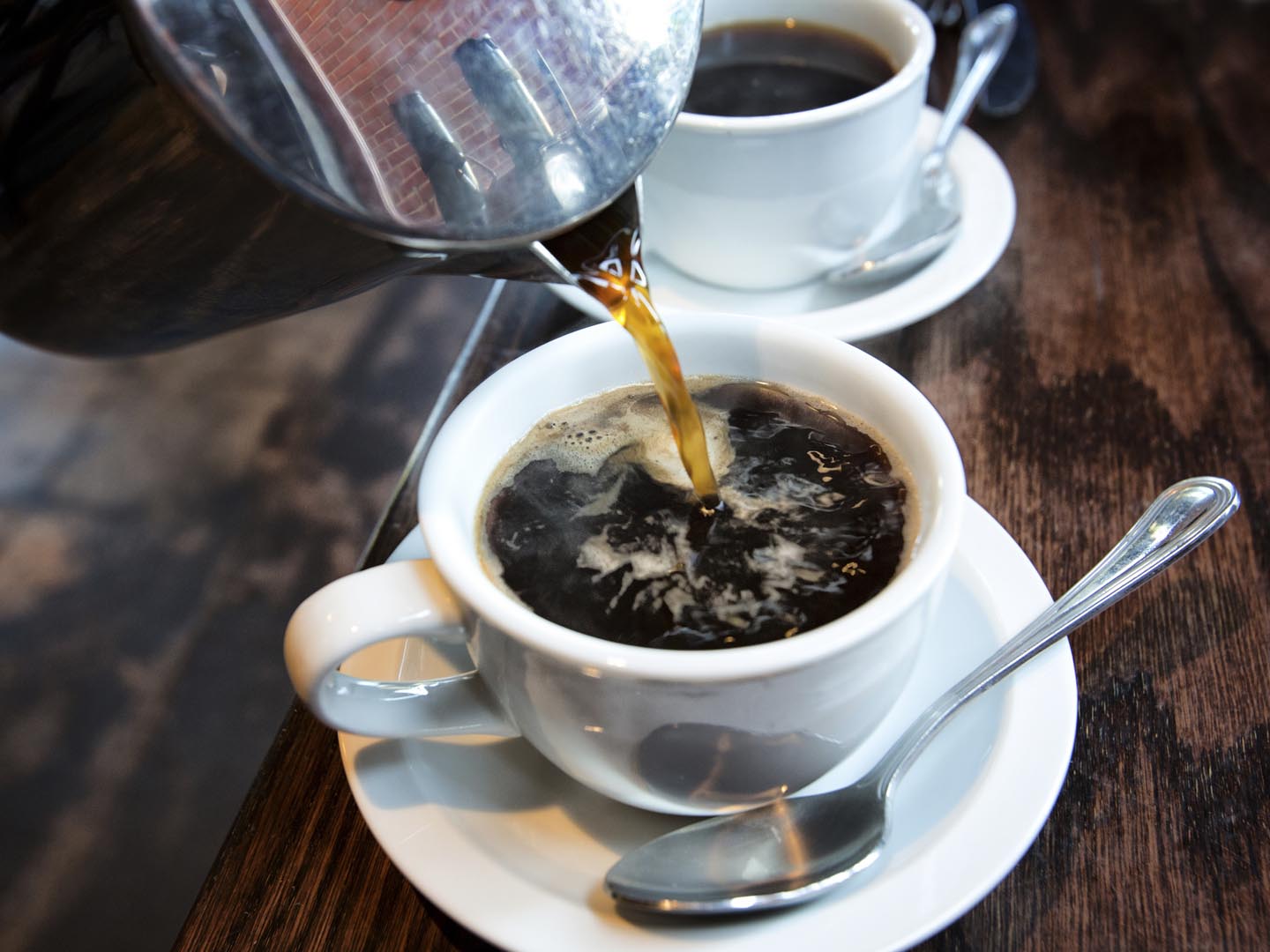 在一家时髦的咖啡馆里，新鲜的热咖啡正从不锈钢法式压壶里倒进杯子里