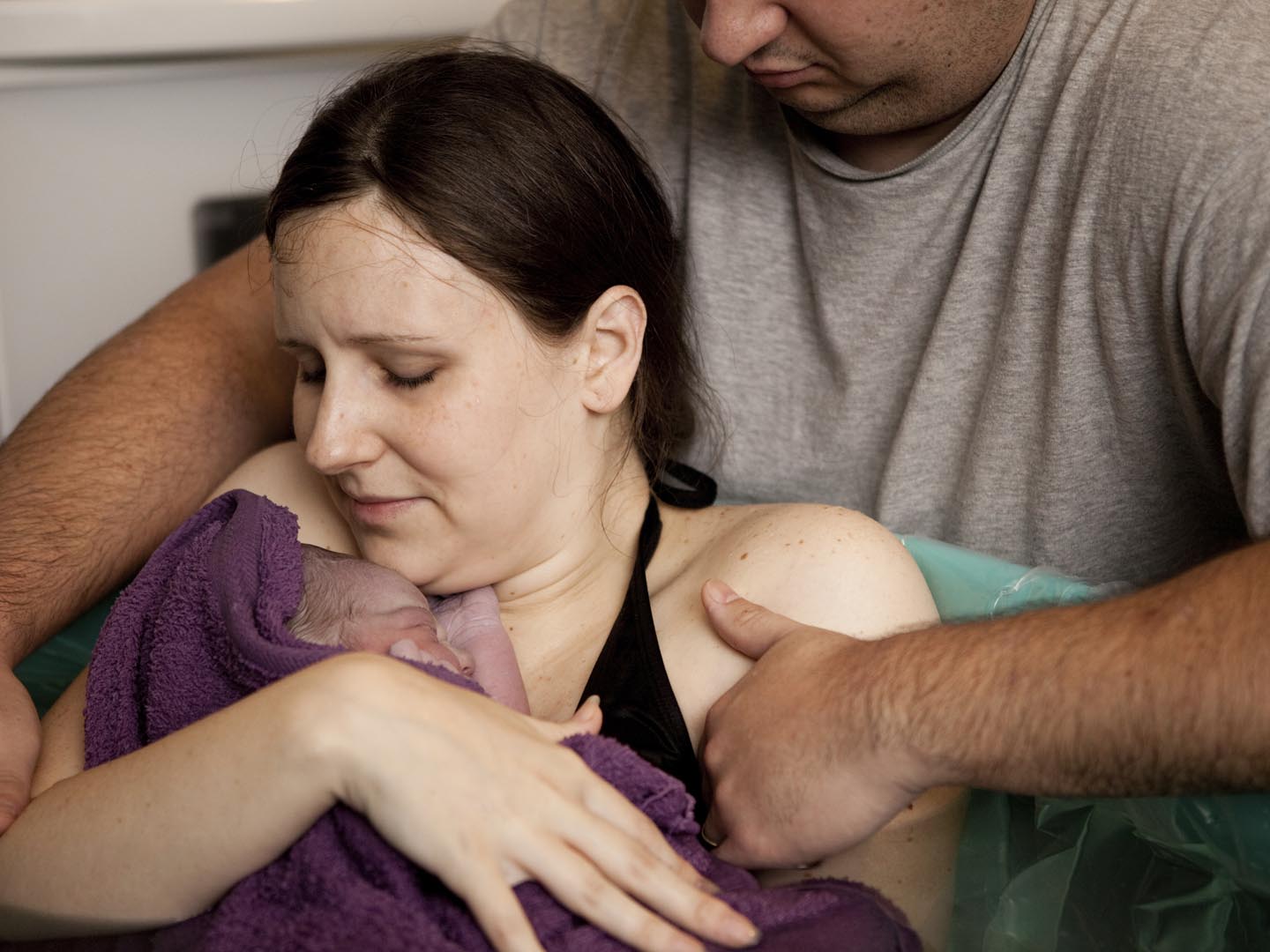 彩色照片，丈夫安慰他的妻子，而她抱着他们的新生儿在水中分娩后，立即在家里。