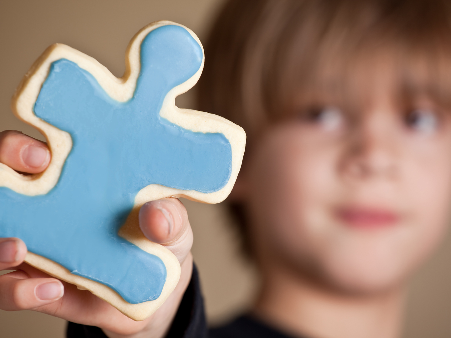 一个9岁的小男孩拿出一块蓝色的冰镇拼图形状的糖饼干。浅景深，只关注cookie。四月是自闭症宣传月。五颜六色的拼图通常用来代表对自闭症的认识。在美国，每88名儿童中就有1名被诊断为ASD(自闭症谱系障碍)。