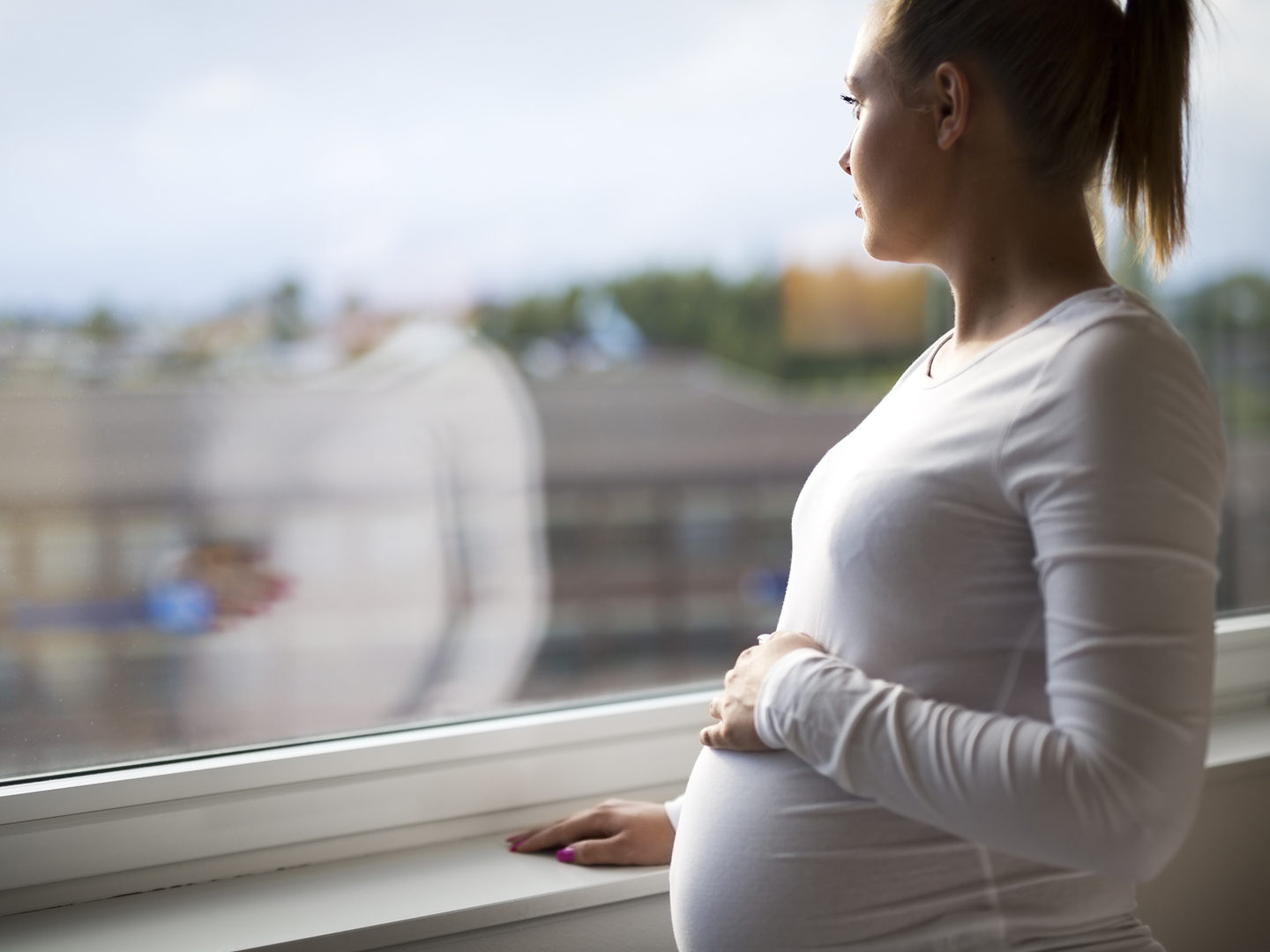 体贴的孕妇望着窗外回家。一只手放在肚子上。心理健康和怀孕。