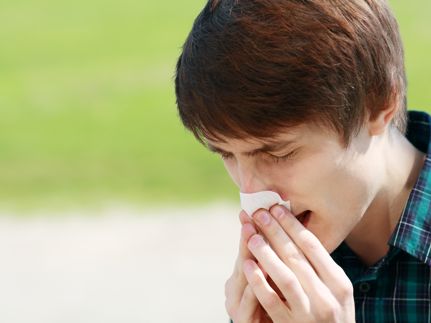 年轻人在户外打喷嚏和擤鼻涕，因为他有过敏。