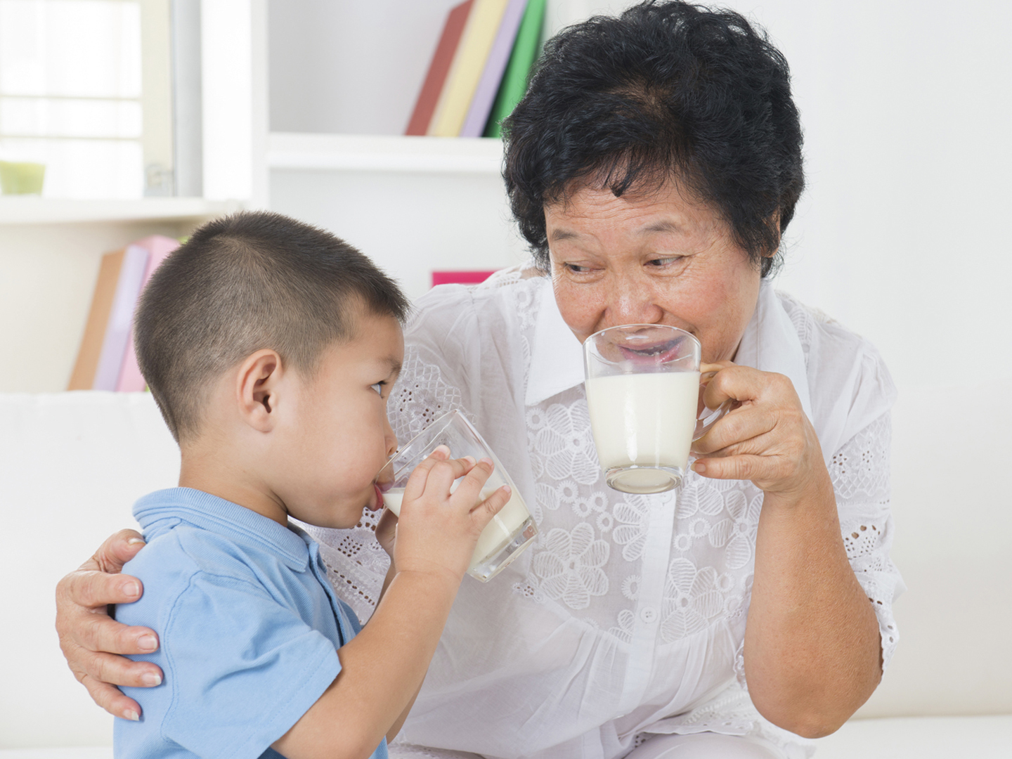 喝牛奶。快乐的几代亚洲家庭在家里喝牛奶。美丽奶奶和孙子，保健理念。