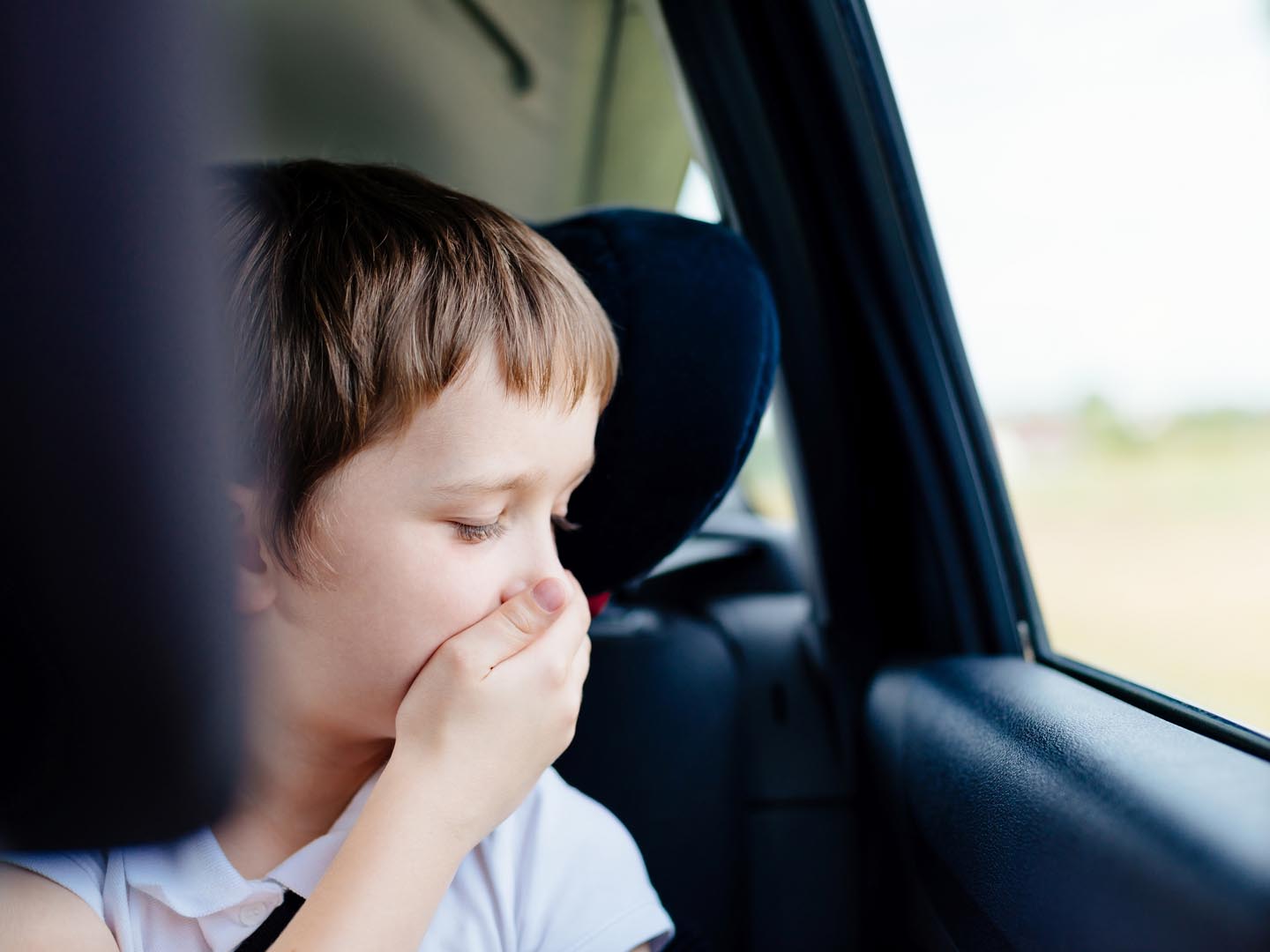 7岁的小孩坐在汽车后座上，坐在儿童安全座椅上，用手捂住嘴——患有晕动病