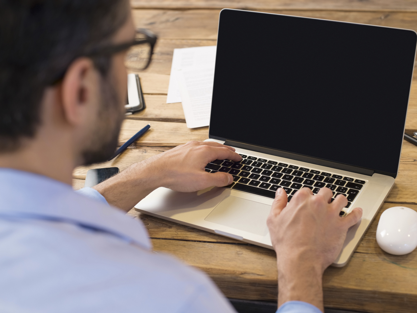 背面的商人坐在笔记本电脑屏幕前。一名男子在办公室用现代笔记本电脑打字。年轻的学生坐在木桌前用电脑打字。