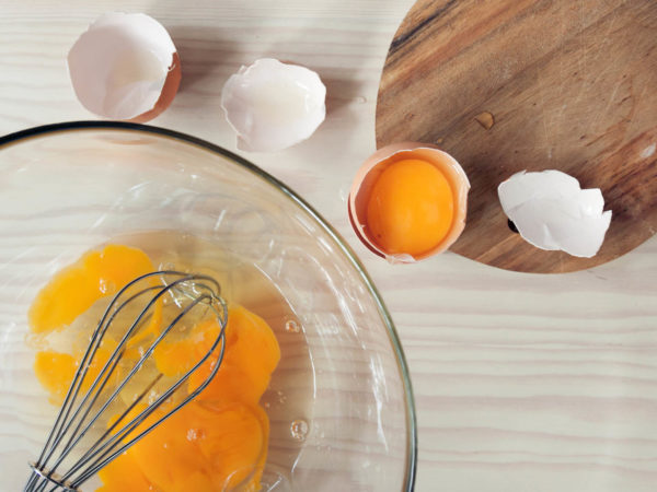 用打蛋器把鸡蛋放在碗里，放在木制厨房柜台上。