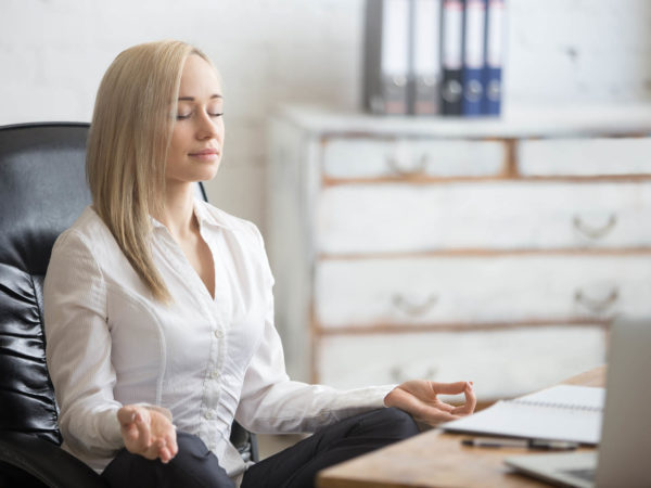 商业和健康的生活方式理念。画像年轻的办公室妇女坐在轻松的瑜伽姿势在工作场所盘腿。微笑的商务女士在休息时间沉思
