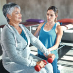 一位老年妇女在理疗师的帮助下使用举重和健身球的镜头