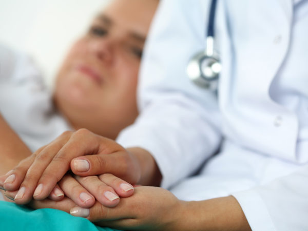 友好的女医生手牵病人的手躺在床上，在体检时给予鼓励、同情、欢呼和支持。减少坏消息、同情、信任和伦理观念