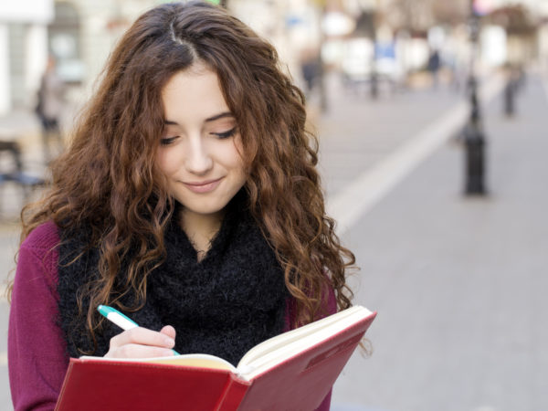 十几岁的女学生站在步行街上，在笔记本上写字