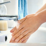 侧视图无法辨认的白人妇女在浴室用肥皂洗手。水漫过她的双手，背景中可见蓝色的凹陷。