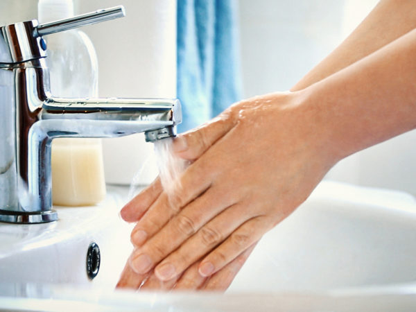 不知名的白人妇女在浴室用肥皂洗手的侧视图。水正浇在她的手上，背景中可见蓝色的水槽。
