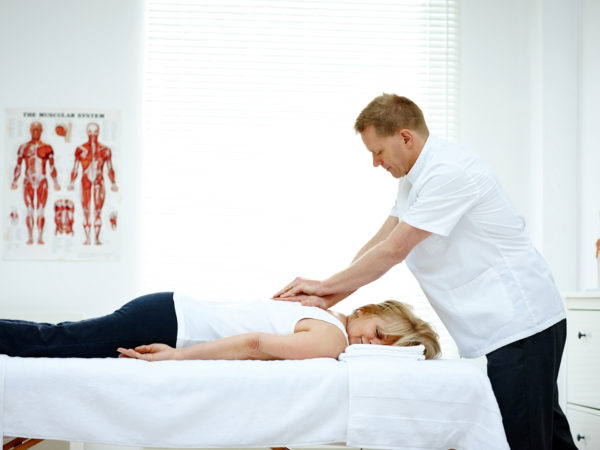 男性整骨医生治疗背部问题的妇女躺在医疗室