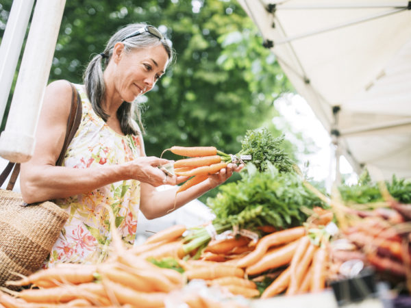 一位50多岁的老妇人在当地农贸市场购买新鲜的有机蔬菜。她微笑着选择胡萝卜。具有复制空间的水平图像。
