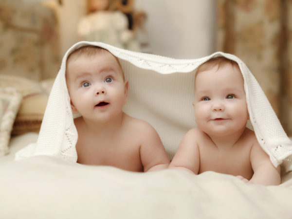 两个双胞胎婴儿，七个月的微笑女孩盖着白毛巾在床上白色的床单