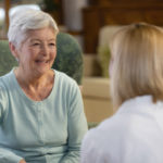 正面，微笑的老年病人坐在扶手椅上与家庭保健护士或女医生交谈，背面。